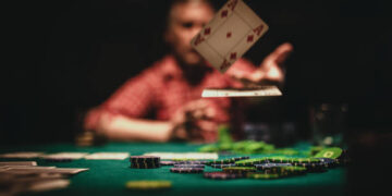 One mature man playing poker late by night, throwing playing cards on table.
